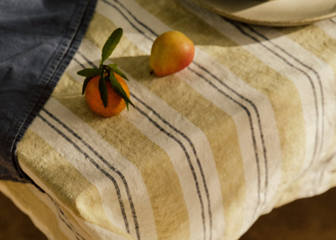 A striped tablecloth with fruit, a plate and a denim tea towel