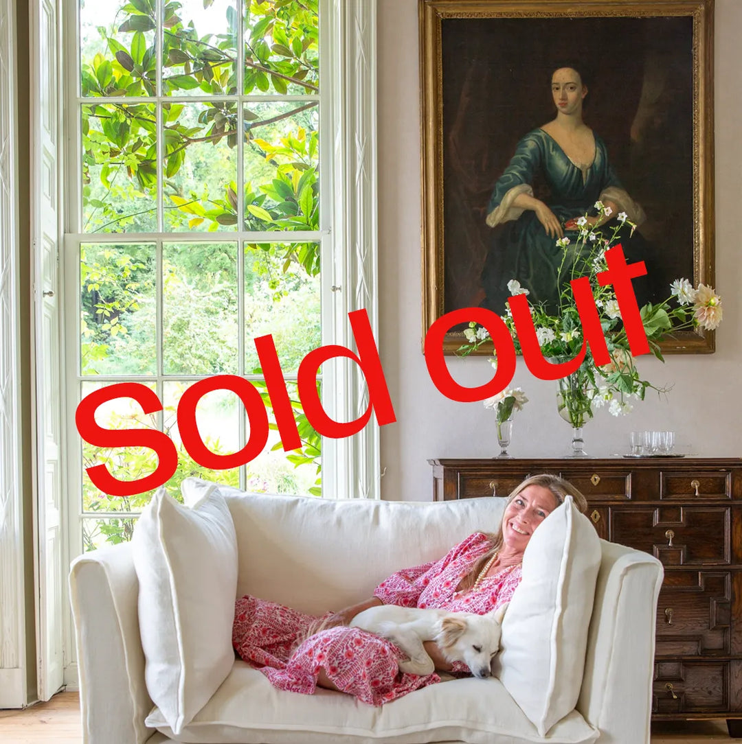 Sophie lying on a white sofa with a dog, surrounded by decor including a painting and flowers.