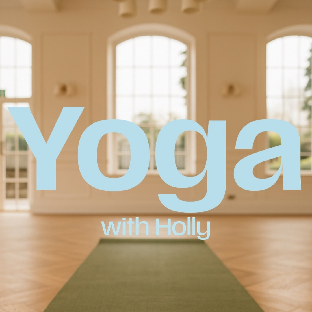A large light blue text overlay reading 'Yoga with Holly' is centered over a softly blurred indoor studio scene with tall arched windows, warm beige walls, wooden flooring, and a green yoga mat on the floor.